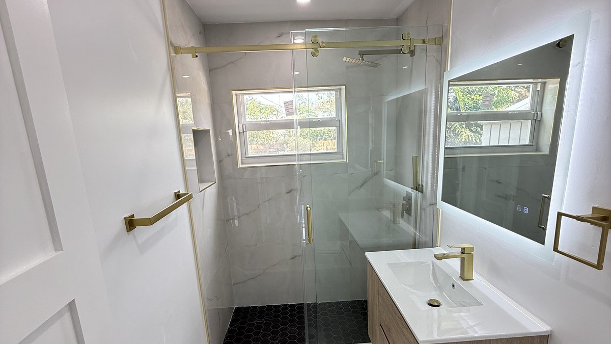 Walk-in shower with gold fixtures next to a floating wood vanity