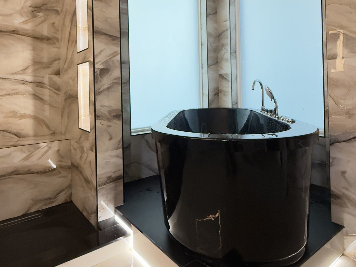 Freestanding black soaking tub with crystal chandelier and marble walls